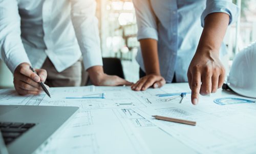 Two architect working at construction site and compass drawing pointing on blueprint with partnership.